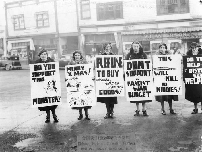 Black and white photograph showing a group of women in Vancouver, BC, standing in the street carrying placards. The women seem to be protesting against the war and advocate for the boycott of Japanese, German and Italian goods.
